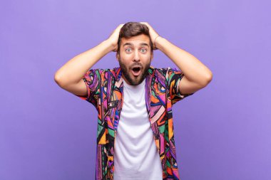 Genç adam heyecanlı ve şaşırmış görünüyor, ağzı açık, elleri başının üstünde, şanslı bir kazanan gibi hissediyor.