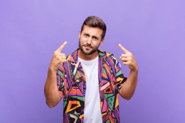 Kötü tavırlı genç adam gururlu ve agresif görünüyor, yukarıyı işaret ediyor ya da elleriyle alay işareti yapıyor.