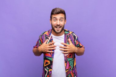 Genç adam mutlu görünüyor, şaşırmış, gururlu ve heyecanlı, kendini işaret ediyor.