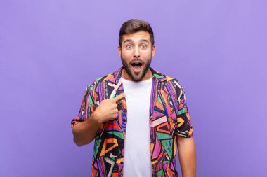 Şok olmuş ve ağzı açık, kendini işaret eden genç bir adam.