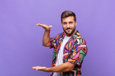 Delikanlı iki eli yanda olan bir objeyi tutuyor fotokopi alanı, bir nesneyi gösteriyor, sunuyor ya da reklamını yapıyor.