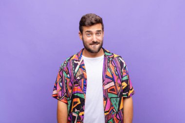 Genç adam şaşkın ve şaşkın görünüyor, gergin bir hareketle dudağını ısırıyor, sorunun cevabını bilmiyor.