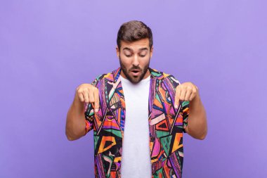 İki eliyle aşağıya bakan ağzı açık genç bir adam, şaşkın, şaşkın ve şaşırmış görünüyor.