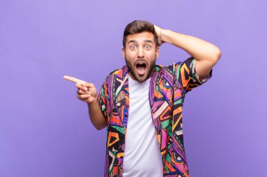 Genç adam gülüyor, mutlu, pozitif ve şaşırmış görünüyor. Yan fotokopi alanını işaret eden harika bir fikrin farkına varıyor.