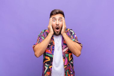 Genç adam mutsuz, korkmuş ya da endişeli görünüyor, ağzı sonuna kadar açık ve iki kulağını da elleriyle kapatıyor.