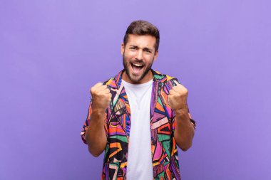 Genç adam muzaffer bir şekilde bağırıyor, gülüyor, mutlu ve heyecanlı hissediyor.