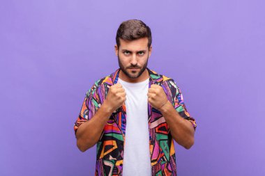 Genç adam kendinden emin, sinirli, güçlü ve agresif görünüyor. Yumrukları boks pozisyonunda dövüşmeye hazır.