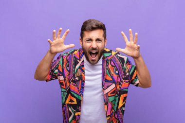 Genç adam panik ya da öfke içinde bağırıyor. Şok olmuş, korkmuş ya da öfkeli. Elleri başının yanında.