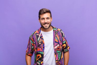 Genç adam neşeli bir şekilde gülümsüyor. Olumlu, mutlu, kendinden emin ve rahat bir ifadeyle.