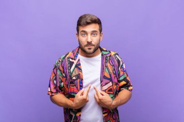 Genç adam şaşkın ve şaşkın bir bakışla kendini işaret ediyor. Seçildiğine şaşırmış ve şaşırmış.