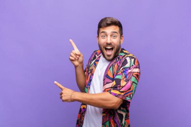 Genç adam sevinçli ve şaşırmış hissediyor, şok olmuş bir ifadeyle gülümsüyor ve bir tarafı işaret ediyor.