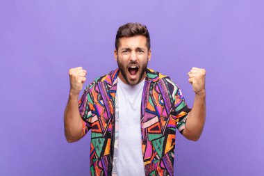 Genç adam öfkeli bir ifadeyle ya da yumruklarıyla başarıyı kutlarken agresif bir şekilde bağırıyor.