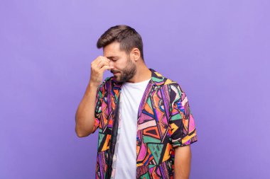 Genç adam stresli, mutsuz ve hayal kırıklığına uğramış, alnına dokunuyor ve şiddetli baş ağrısı çekiyor.