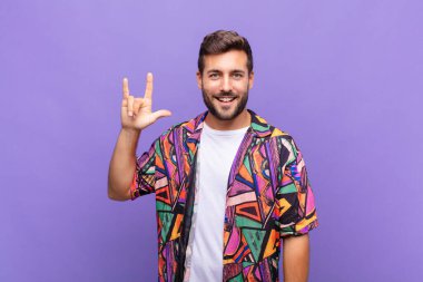 Genç adam mutlu, eğlenceli, kendinden emin, pozitif ve asi hissediyor, elle kaya veya heavy metal işareti yapıyor.