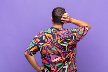 Genç adam bilgisiz ve kafası karışık, bir çözüm düşünüyor, eli kalçasında, diğeri kafasında, dikiz aynasından.