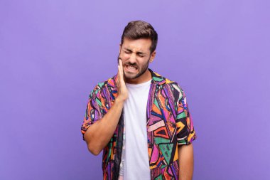 Yanak tutan ve acı çeken diş ağrısı çeken genç adam hasta, sefil ve mutsuz hisseden, dişçi arayan.