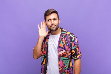 Genç adam ciddi ve meraklı görünüyor, dinliyor, gizli bir konuşma ya da dedikodu duymaya çalışıyor, gizlice dinliyor.