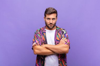 Genç adam mutsuz ve hayal kırıklığına uğramış, ciddi görünüyor, sinirlenmiş ve kollarını kavuşturmuş.