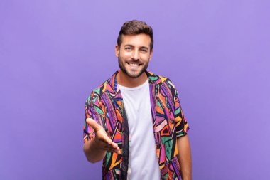 Genç adam gülümsüyor, mutlu görünüyor, kendinden emin ve arkadaş canlısı, bir anlaşma yapmak için el sıkışma teklif ediyor, işbirliği yapıyor.
