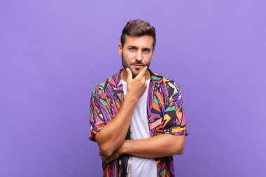 Genç adam ciddi görünüyor, düşünceli ve güvensiz, bir kolu çapraz ve çene üzerinde, seçenekleri tartıyor