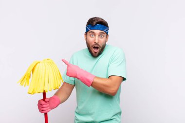 Genç adam mutlu, şaşkın ve şaşırmış hissediyor. Ağzını eliyle kapatıyor ve yanal fotokopi alanını işaret ediyor.