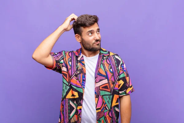 Genç adam şaşkın ve şaşkın hissediyor, başını kaşıyor ve yana bakıyor.