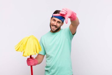 Genç adam mutlu, arkadaş canlısı ve pozitif hissediyor, gülümsüyor ve elleriyle bir portre veya fotoğraf çerçevesi yapıyor.