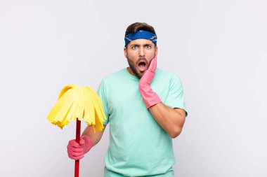 Genç adam şok ve inançsızlık içinde, elleri yanak ve kolları çapraz, sersemlemiş ve şaşırmış hissediyor.