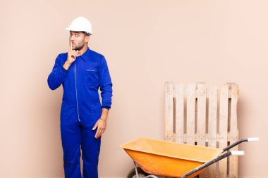 Genç adam sessizlik ve sessizlik istiyor, parmağıyla ağzının önünde işaret ediyor, 