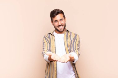 Genç adam mutlu bir şekilde gülümsüyor arkadaş canlısı, kendinden emin, pozitif bakışlı, bir nesne ya da konsept sunuyor ve gösteriyor
