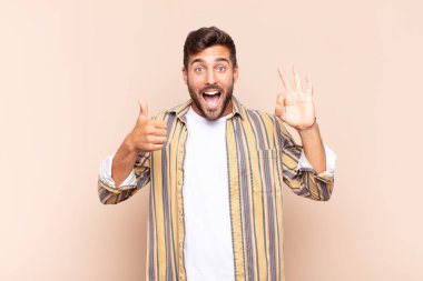 Genç adam mutlu, şaşkın, tatmin olmuş ve şaşırmış hissediyor, iyi görünüyor ve el hareketlerini gösteriyor, gülümsüyor.