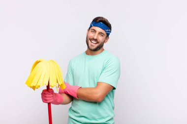 Genç adam kollarını kavuşturup mutlu bir şekilde gülüyor, rahat, pozitif ve tatmin olmuş bir şekilde.