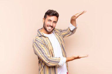 Genç adam gülümsüyor, mutlu, pozitif ve tatmin olmuş hissediyor, fotokopi alanında nesne veya konsept tutuyor veya gösteriyor