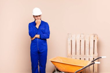 Genç adam ciddi, düşünceli ve endişeli, elleri çene inşaatı kavramına bastırılmış şekilde yan bakıyor.