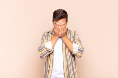 Genç adam üzgün, hayal kırıklığına uğramış, gergin ve depresif, iki eliyle yüzünü kaplayan, ağlayan