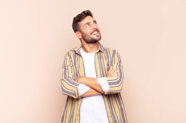 Genç adam mutlu, gururlu ve umutlu, merak ediyor ya da düşünüyor, çapraz kollarla uzayı taklit ediyor.