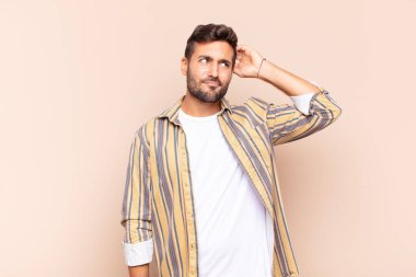 Genç adam şaşkın ve şaşkın hissediyor, başını kaşıyor ve yana bakıyor.