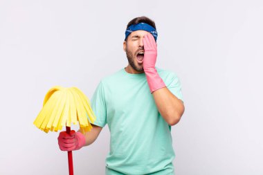 Genç adam uykulu, sıkılmış ve esniyor, baş ağrısı ve yüzünün yarısını kaplayan bir elle.