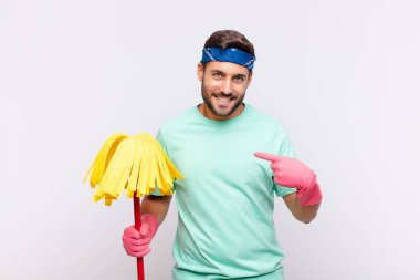 Genç adam gururlu, kendinden emin ve mutlu görünüyor, gülümsüyor ve kendini işaret ediyor veya bir numaralı işareti yapıyor.