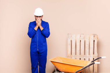 Genç adam mutlu, neşeli, şanslı ve şaşırmış görünüyor. İki eli inşaat konseptiyle ağzını kapatıyor.