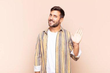 Genç adam mutlu ve neşeyle gülümsüyor, el sallıyor, seni selamlıyor ve selamlıyor, ya da hoşça kal diyor.