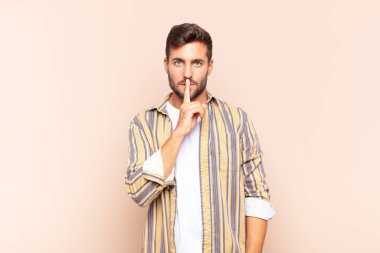 Genç adam ciddi görünüyor ve parmaklarını dudaklarına bastırıp sessizlik ya da sessizlik talep ediyor, sır saklıyor.