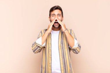 Genç adam mutlu, heyecanlı ve pozitif hissediyor. Elleri ağızda, bağırıyor.