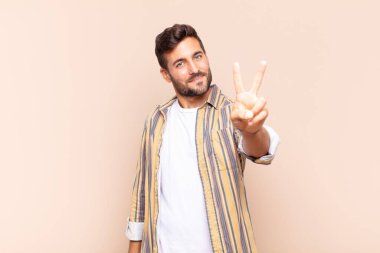 Genç adam gülümsüyor ve mutlu görünüyor, kaygısız ve pozitif, tek elle zafer ya da barış işareti yapıyor.