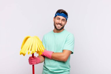 Genç adam mutlu, gururlu ve memnun görünüyor. Kollarını kavuşturup gülümsüyor.