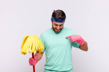 Genç adam neşeyle gülümsüyor, yere bakıyor ve göğsüne işaret ediyor.