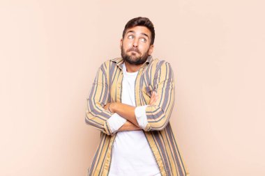 Genç adam omuz silkiyor, kafası karışık ve kararsız, kolları bağlı ve şaşkın bir şekilde şüpheli bakıyor.