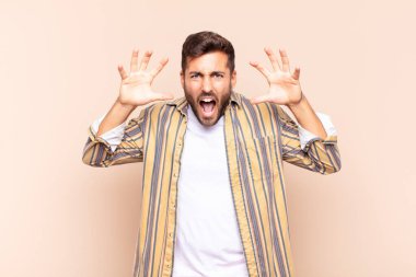 Genç adam panik ya da öfke içinde bağırıyor. Şok olmuş, korkmuş ya da öfkeli. Elleri başının yanında.