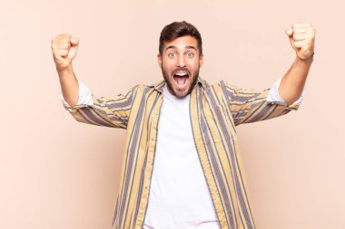 Genç adam muzaffer bir şekilde bağırıyor, heyecanlı, mutlu ve şaşırmış görünüyor.