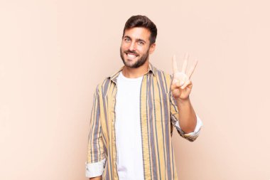 Genç adam gülümsüyor ve arkadaş canlısı görünüyor, üç ya da üç numarayı gösteriyor, eli önde, geriye doğru sayıyor.